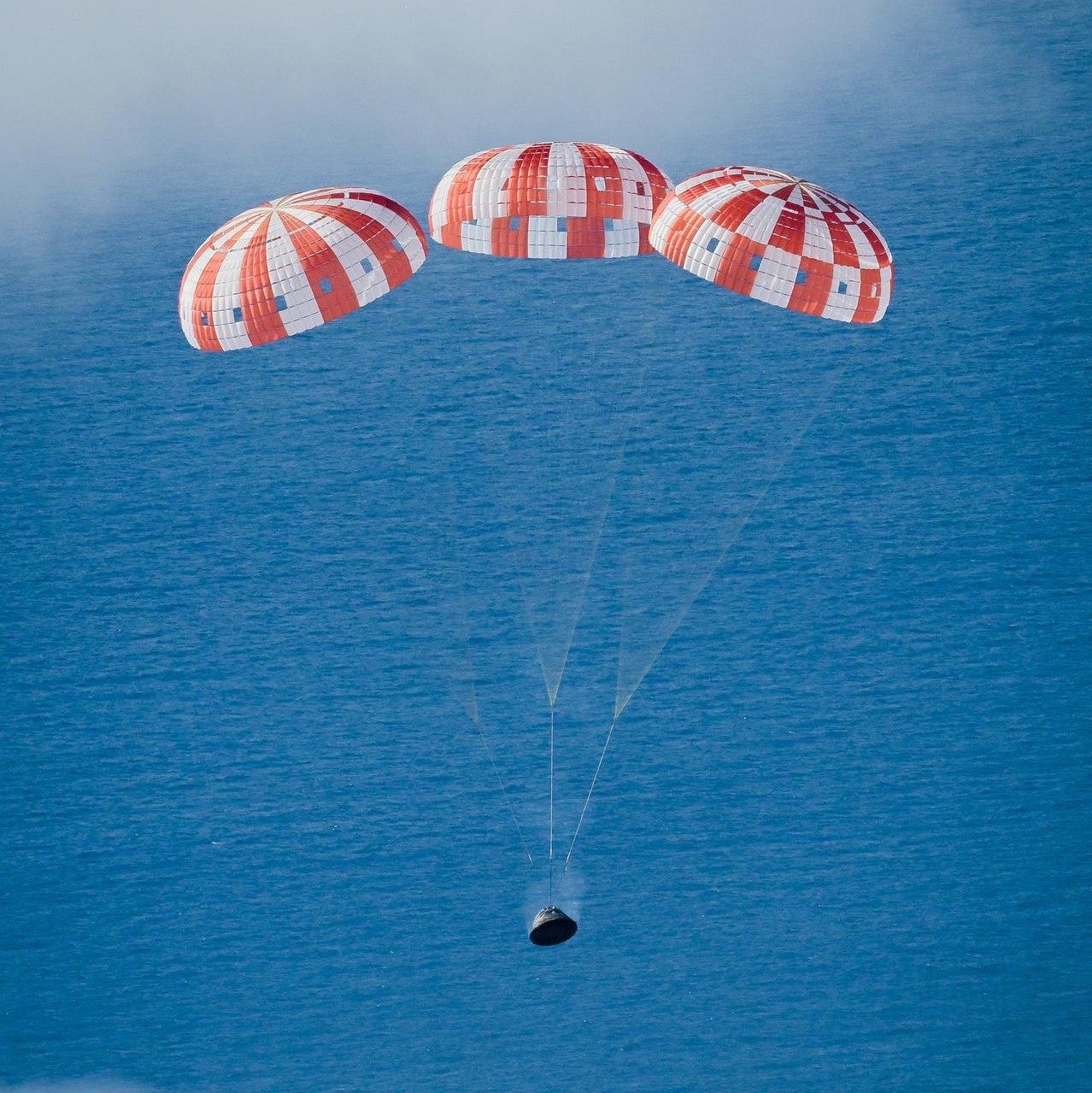 Orion under three opened parachutes descending toward the ocean for splashdown